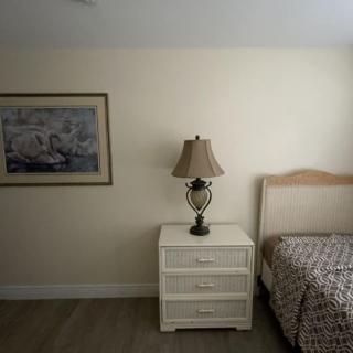 A cozy bedroom corner featuring a bedside table with a lamp, a bed, and wall art.