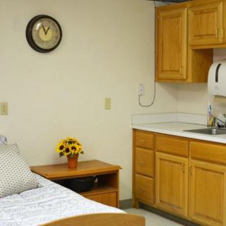 A cozy room featuring a bed, wooden cabinets, and a small sink area with wall clock decor.