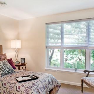 A cozy bedroom with a large window, decorated with patterned bedding and soft lighting.