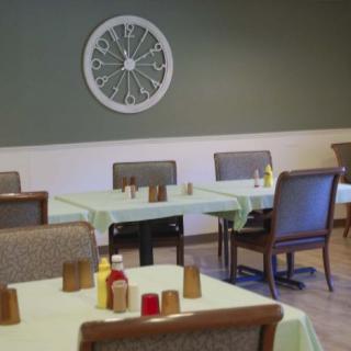 An empty dining room with neatly arranged tables and chairs, featuring a decorative wall piece.