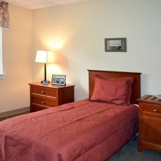 A cozy bedroom with a single bed, wooden nightstands, and a lamp.