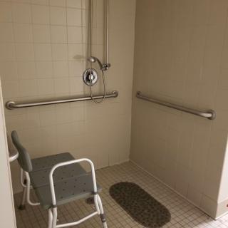 An accessible shower equipped with grab bars, a shower chair, and a non-slip mat for safety.