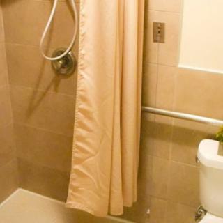 A bathroom with a shower area, curtain, toilet, and grab bar.