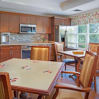 A modern kitchen and dining area with wooden cabinets, a microwave, refrigerator, and several dining tables and chairs.