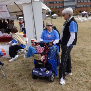 A group of people interacting at an outdoor event, with one person seated in a wheelchair.