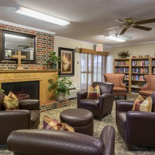 A cozy living room with armchairs around a fireplace and bookshelves.