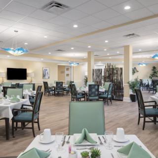 An elegant dining room with neatly arranged tables and chairs, set with place settings under warm lighting.
