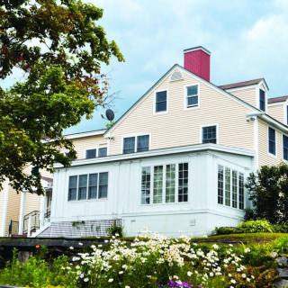 A large residential house with a red chimney, surrounded by a lush garden and trees.