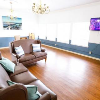 A spacious living room featuring comfortable sofas, a chandelier, and a mounted television.