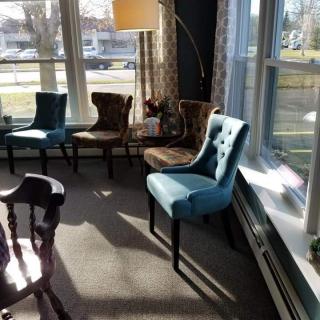A sunlit living room with various chairs arranged near large windows.