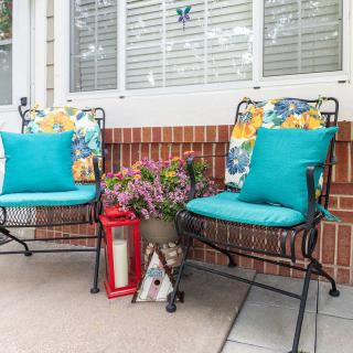 A cozy patio setup with colorful cushions on wrought iron chairs, accompanied by flowers and a red lantern.