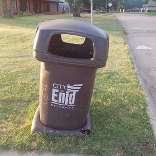 A public trash can designed for waste disposal in a park setting.
