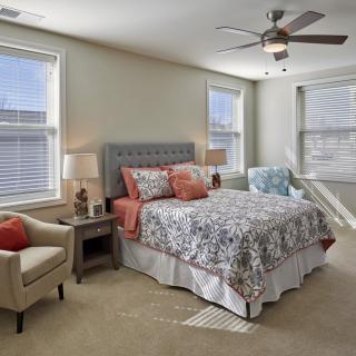 A cozy and well-lit bedroom with a stylish bed and patterned bedding, complemented by natural light from multiple windows.