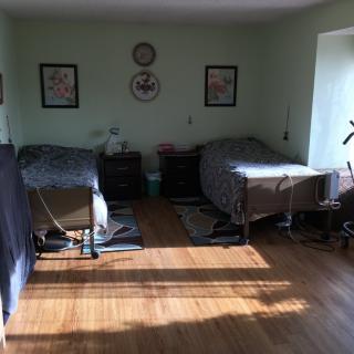 A cozy bedroom with two beds, sunlight streaming in, and decorative elements on the wall.