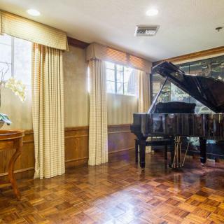 A cozy music room featuring a grand piano on a parquet floor, adorned with curtains and wood paneling.