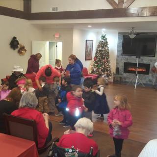 A festive gathering with children and adults celebrating around a Christmas tree indoors.