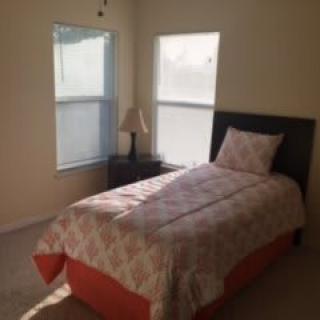 A simple, sunlit bedroom with a single bed and bedside lamp.