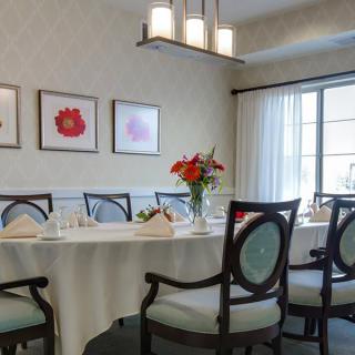 A well-decorated dining room with a large table, elegant chairs, floral centerpiece, and wall art under natural lighting.
