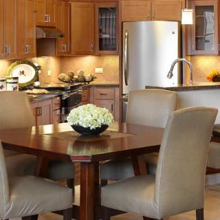 A modern kitchen and dining area with wooden cabinets, a stainless steel refrigerator, and a central table with upholstered chairs.