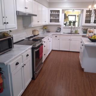 A modern kitchen with white cabinets, a hardwood floor, and various appliances.