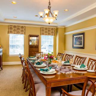 A warmly decorated dining room with a large wooden table set for a meal, surrounded by elegant chairs and illuminated by a chandelier.