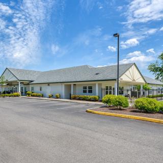 A single-story building with a parking lot under a blue sky with clouds.