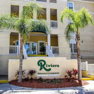 Entrance to the Riviera apartment complex with palm trees and landscaping.