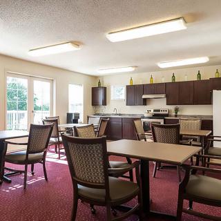 A spacious communal kitchen and dining area with several tables and chairs, featuring large windows and modern appliances.