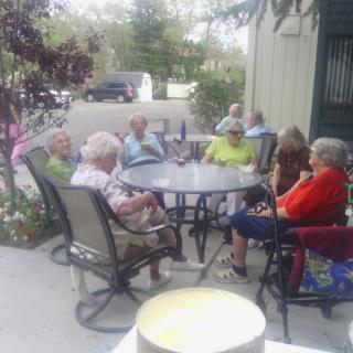 A group of seniors sitting around a table outdoors, engaged in conversation.