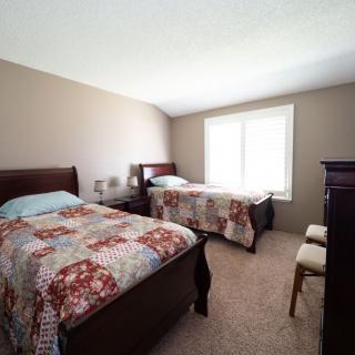 A cozy bedroom with two twin beds and a carpeted floor, well-lit by a large window.