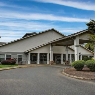 A modern building entrance with a circular driveway and landscaped surroundings under a partly cloudy sky.