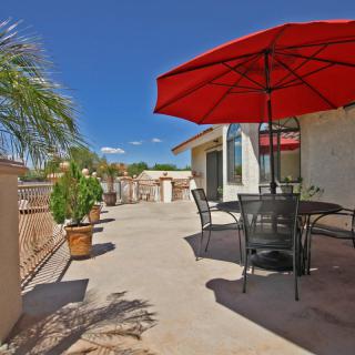 A spacious outdoor patio with a red umbrella, metal furniture, and potted plants under a clear blue sky.