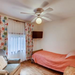 A cozy bedroom with a single bed, floral curtains, and a ceiling fan.