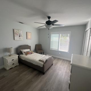 A modern bedroom with minimalistic decor, featuring a bed, a nightstand, a dresser, and a ceiling fan.
