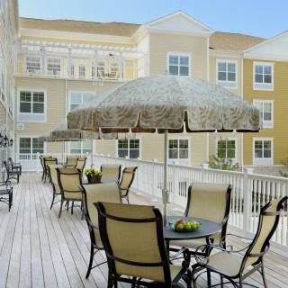 An outdoor patio area with tables, chairs, and umbrellas in front of a residential building.