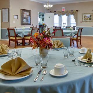 An elegantly set dining table in a spacious restaurant with floral centerpiece and neatly arranged utensils.