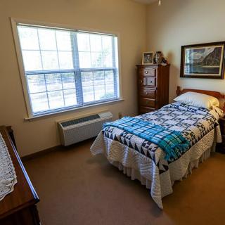A cozy bedroom with a single bed, featuring a colorful quilt and a dresser by the window.
