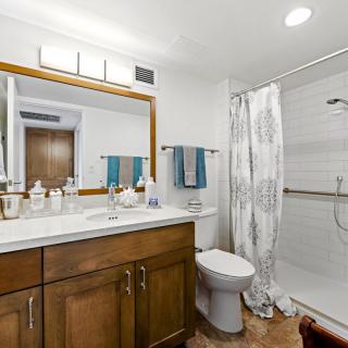 A modern bathroom with a wooden vanity, large mirror, and walk-in shower.
