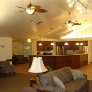 An open-plan living area with a kitchen and seating arrangement, featuring ceiling fans and cozy lighting.