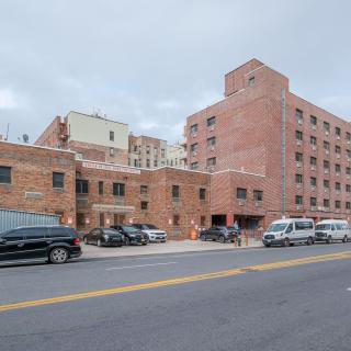 A brick building with parked vehicles along an urban street on an overcast day.