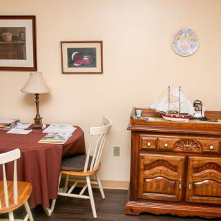 A cozy dining room with a round table, chairs, and wooden sideboard adorned with a model ship.