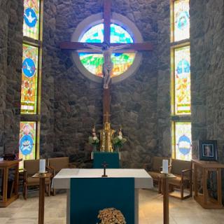 A serene interior of a church featuring a prominent cross, an altar, and beautifully designed stained glass windows.