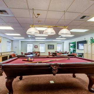 A recreation room with a pool table and cozy seating area, featuring overhead lighting and decor.