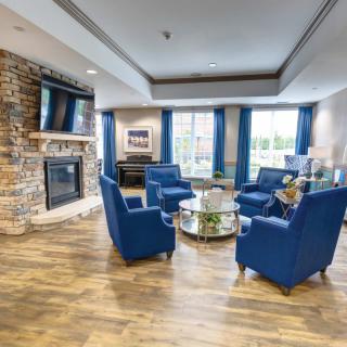 A cozy living room with blue chairs arranged around a coffee table, featuring a stone fireplace and wood flooring.