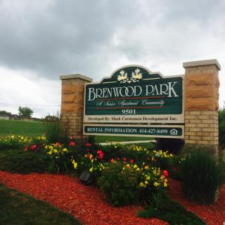Entrance sign of Brentwood Park surrounded by flowers on a cloudy day.