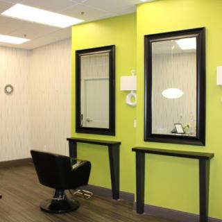 A modern salon interior featuring two mirrors and stylish black chairs against a vibrant green wall.