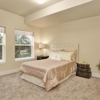 A cozy bedroom featuring a neatly made bed, soft carpets, and large windows allowing natural light to fill the room.