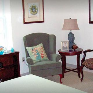 A cozy living room corner featuring an armchair, side table with a lamp, and framed artwork on the walls.
