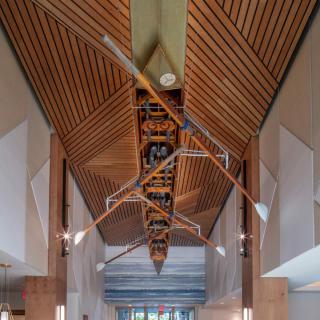 A sleek architectural interior featuring a wooden ceiling adorned with a suspended boat and oars.