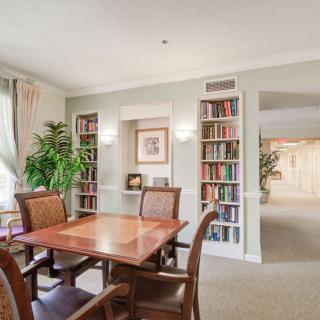 A cozy library room with bookshelves, a table, chairs, and indoor plants.